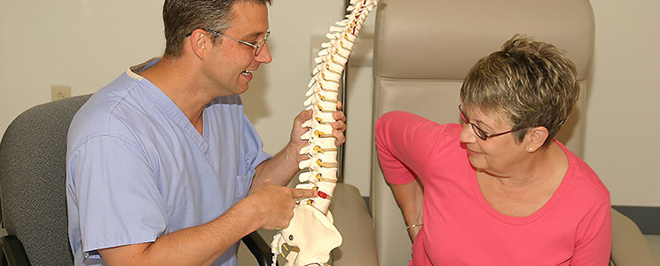 A doctor holding a model of the human spine while talking to a patient